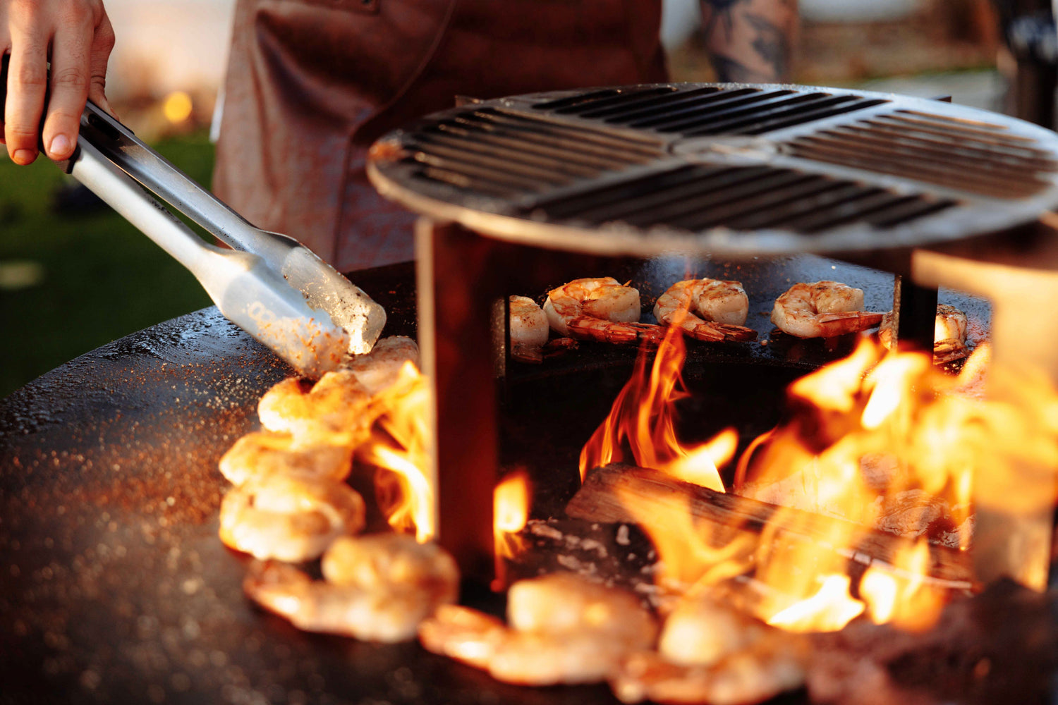 Chef grilling large gambas on the Unifire next to a robust flame, enhancing the seafood with smoky flavors.